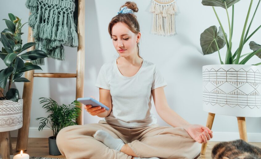 Young healthy woman using phone for setting mobile app for meditation at home,