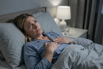 Femme allongée dans son lit la nuit, les mains sur la poitrine, l'air préoccupée par des sensations de vibrations corporelles nocturnes